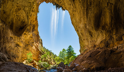 Inside Tonto Natural Bridge in the mountains of Arizona looking out from behind a waterfall.