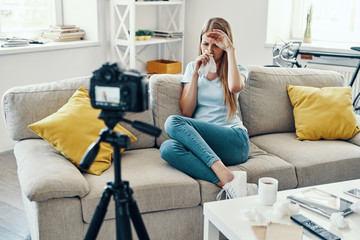 Ill young woman blowing nose while making social media video at home