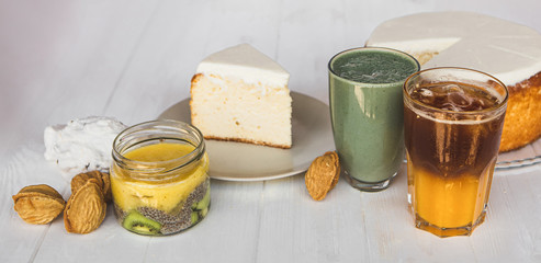 a big white cake  and piece of cake on plate on the background of glasses with drinks on a white wooden table. A concept for a baker's dessert, a cafe, a restaurant