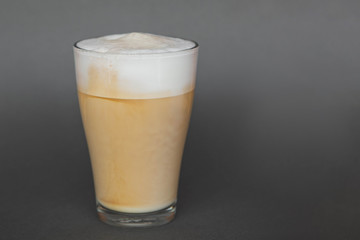 A large transparent glass filled with Latte cooked in a third wave coffee shop is photographed on a gray, isolated background, photo for the menu