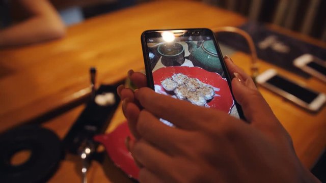 Girl is photographed on a smartphone dessert on a plate and a pot of green tea for your account in the social network.