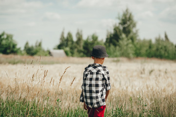 Naklejka na ściany i meble Teenager in hat walk on a summer wheat field. Rural scene. Walking in the farm. Back view