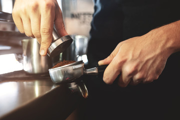 barista holding tamper in one hand going to press ground coffee in holder to make espresso for client in cafe close up