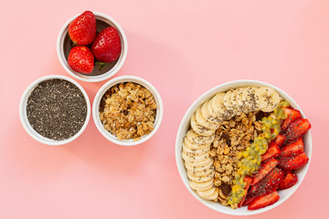 Smoothie bowl with Chia seeds, muesli, strawberries, banana slices and passion fruit on a pink background. Delicious and healthy Breakfast.