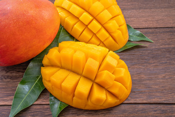 Fresh mango - beautiful chopped fruit with green leaves on dark wood background. Tropical fruit design concept. Flat lay. Top view. Copy space.