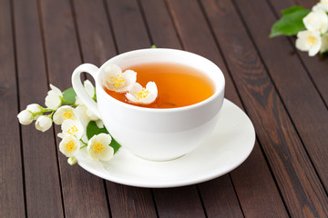 Jasmine tea with jasmine flowers on wooden table background. Cup of hot green tea with jasmine flavor, fresh jasmine flowers. Concept of freshly drink.