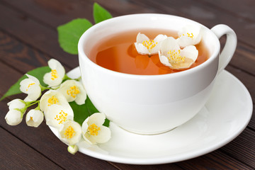 Jasmine tea with jasmine flowers on wooden table background. Cup of hot green tea with jasmine flavor, fresh jasmine flowers. Concept of freshly drink.