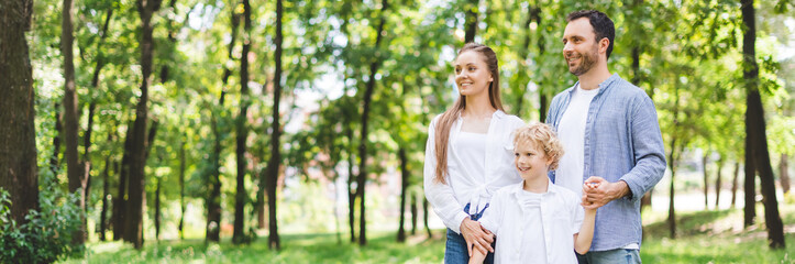 panoramic shot of happy family holding hands in park with copy space