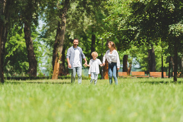 Obraz premium selective focus of happy family holding hands and running in park during daytime