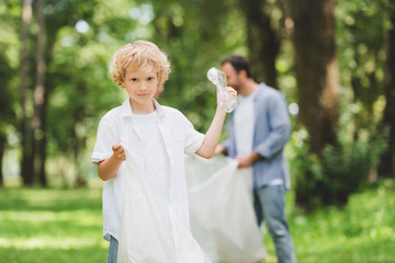 Fototapeta premium adorable boy with plastic bag picking up garbage with father in park