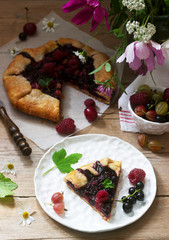 Sweet pie galette with juicy berry filling, berries and wild flowers on a wooden background. Rustic style.