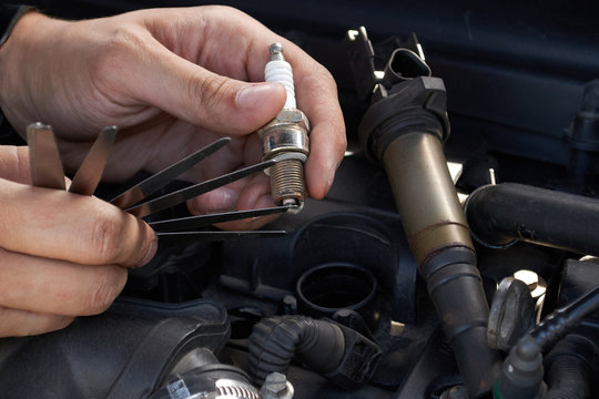 A man checks the spark gap in the spark plug with a probe, close-up