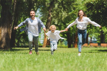Naklejka na ściany i meble smiling family holding hands and running in park during daytime