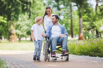 beautiful mother rolling wheelchair with disabled father in park near son