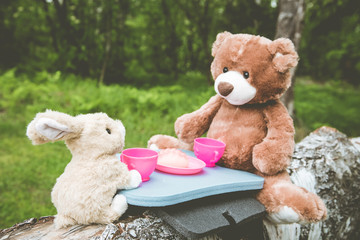 True friends - the rabbit and the little bear are sitting on the grass during a picnic in a park,