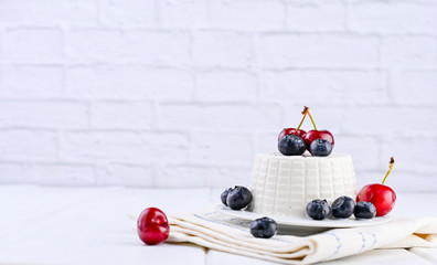 Naklejka na ściany i meble Fresh ricotta cheese with blueberries cherries on a white wooden table. Brick wall on background. Italian dairy product. Homemade breakfast. Healthy food. Copy space.