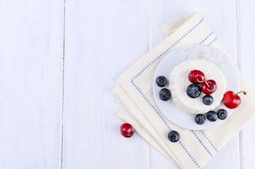 Fresh ricotta cheese with blueberries cherries on a white wooden table. Brick wall on background. Italian dairy product. Homemade breakfast. Healthy food. Copy space.