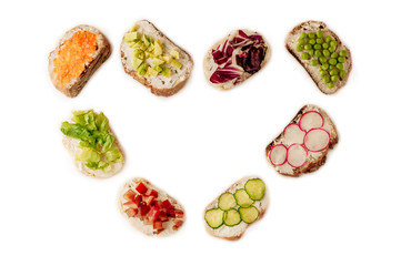 sandwiches or tapas prepared with bread and tasty ingredients. Could be nice food for healthy breakfast ot lunch. Copy space for your text centered in the shape of a heart