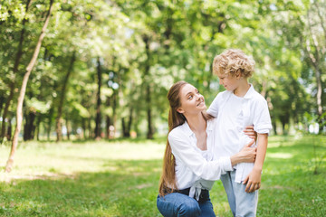 Fototapeta premium beautiful smiling mom hugging son in park during daytime