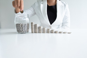 woman hand putting coin into glass bottle bank with coins bar graph, step up growing business to success and saving for retirement concept