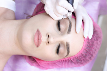 Young woman having permanent makeup on eyebrows in beautician salon	