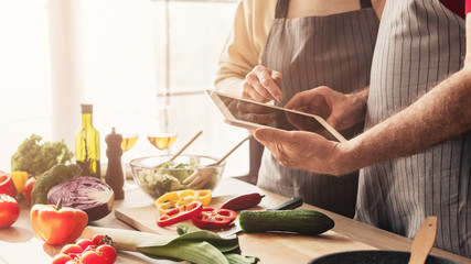 Senior couple searching recipe on digital tablet, cooking at kitchen