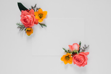 Flat lay bright creative frame of fresh flowers and leaves with white clean blank for text, natural background