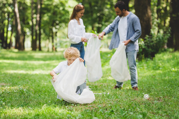 Naklejka na ściany i meble family picking up garbage in plastic bags in park