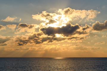 Illuminated by the setting sun clouds over the sea horizon with rays of light and glare on the water.