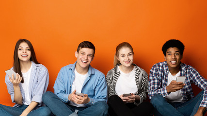 Multiracial teenagers with smartphones looking at camera, orange wall