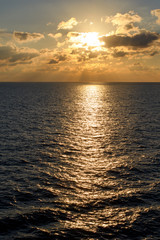 Illuminated by the setting sun clouds over the sea horizon with rays of light and glare on the water.