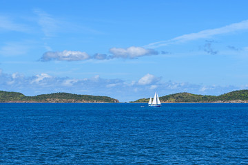 White yacht under a blue sky with clouds on the blue waves of the Caribbean sea against the mountains on the horizon.