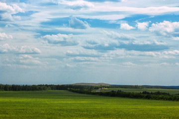 Green field blue sky with clouds and away the track with cars.