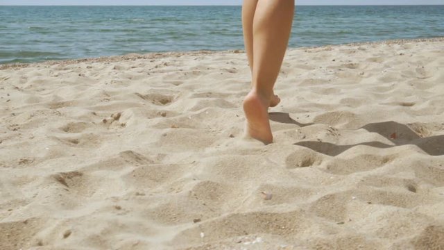 Track shot on the woman's legs while walking in the beach