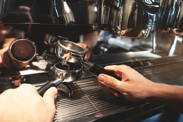 barista man holding two coffee holders one above the other on coffee machine background close up