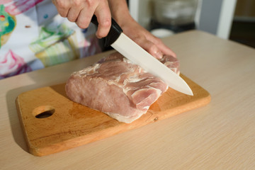 Girl cook cultivates fresh pork meat at home in the kitchen