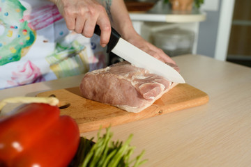Girl cook cultivates fresh pork meat at home in the kitchen