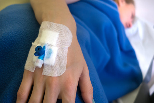 Patient's hand with blue Infusion catheter on blue blanket background. Sick woman with catheter lies on the couch. Catheter closed up