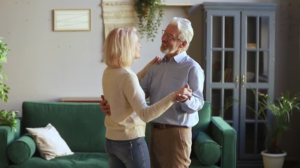 Happy romantic old senior couple dancing waltz in living room