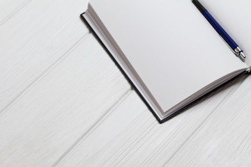 Ballpoint pen in open notebook on a white wooden background. Blank pages in notebook. Ribbed texture of wooden background