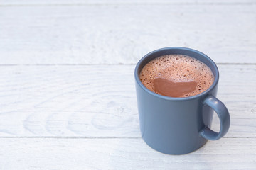 Hot chocolate in a blue-grey ceramic mug isolated on white painted wood. Space for text.