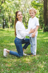 beautiful smiling mom hugging son in park and looking at camera