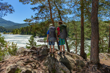 Obraz premium Kids travel hiking in nature. Boys with backpacks look at the mountain river.