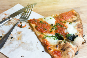 Top view piece fo Pizza with tomatoes, mozzarella, basil and cutlery on served wooden restaurant table. Italian cuisine. Selective focus, copy space