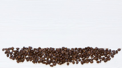 Line of roasted coffee beans down on white wooden background, top view. Copy space, free place for text