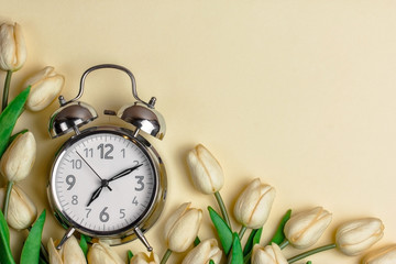 alarm clock on a beige background with white tulips