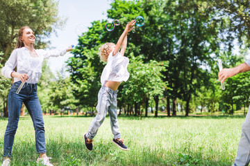 Obraz premium mother, father and son playing with soap bubbles in park