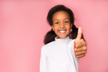 Happy girl showing thumb up on pink background