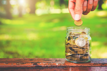 golden coins stack with handsome man hands but coin to jar on wood table with blur nature bokeh background in park. financial saving money concept. ESG Environmental Social Governance. startup.