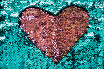 Coral heart made of sequins on turquoise background. Shiny fabric texture